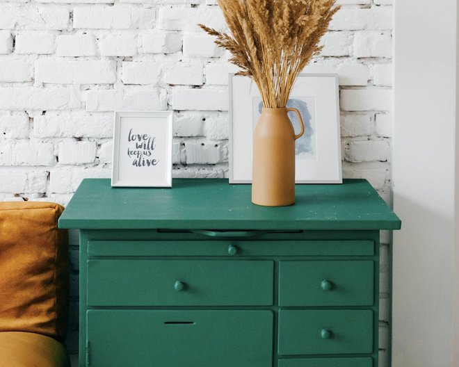 green drawers with vase on top and white brick wall behind